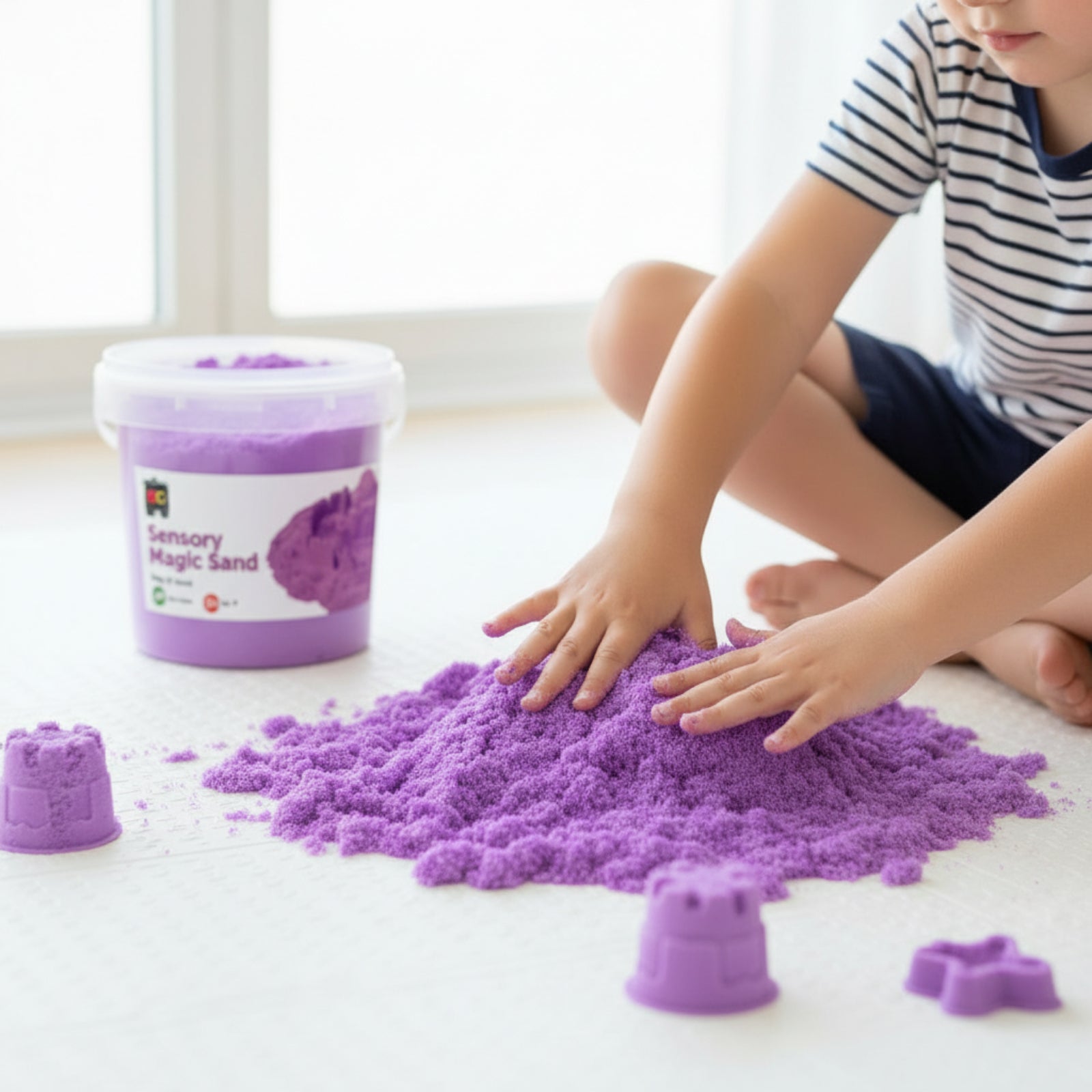 Child using Educational Colours Sensory Magic Sand 1kg Purple during tactile sensory play with moulded sand shapes on floor surface.