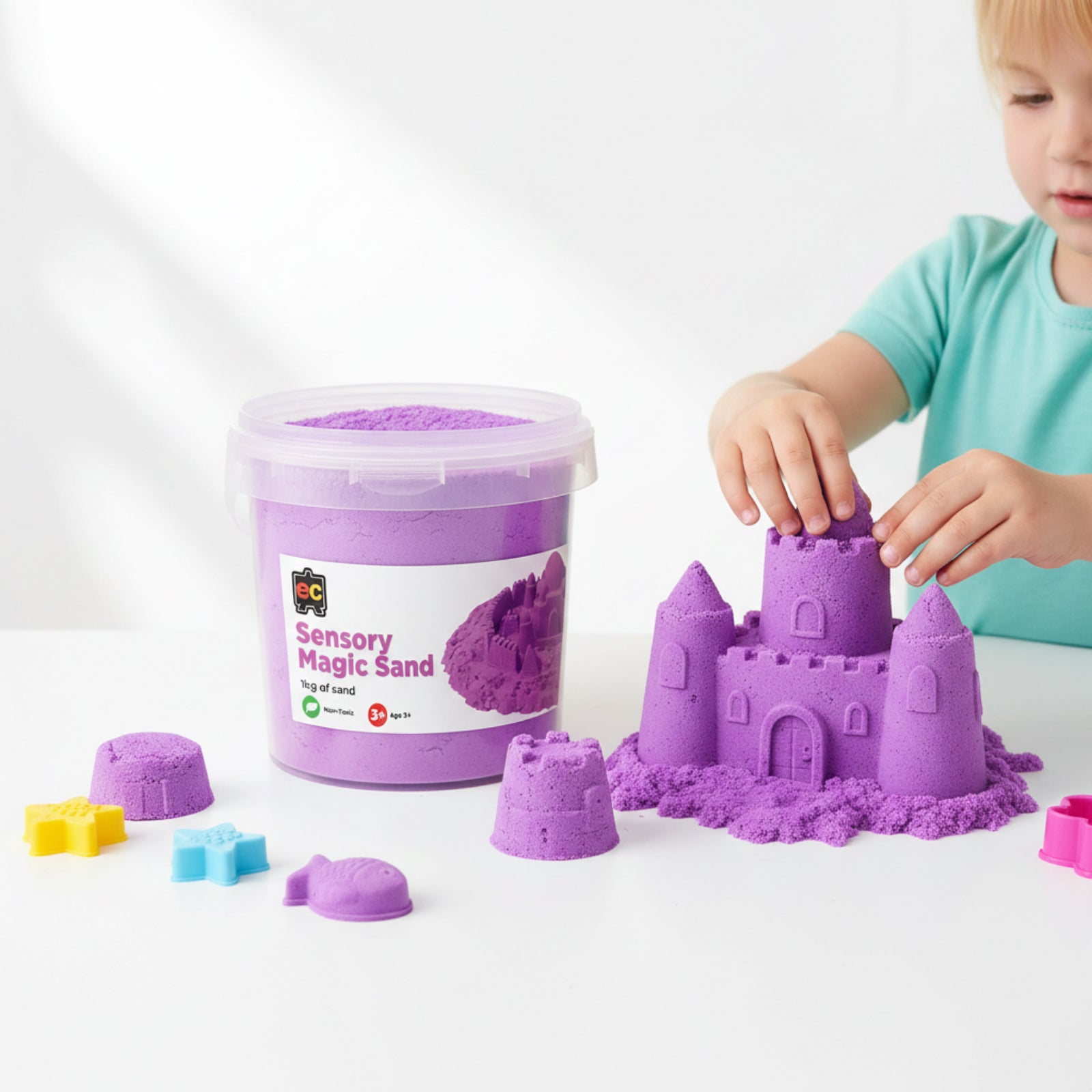 Young child building detailed purple sand castle creations beside Educational Colours Sensory Magic Sand reusable 1kg storage tub.