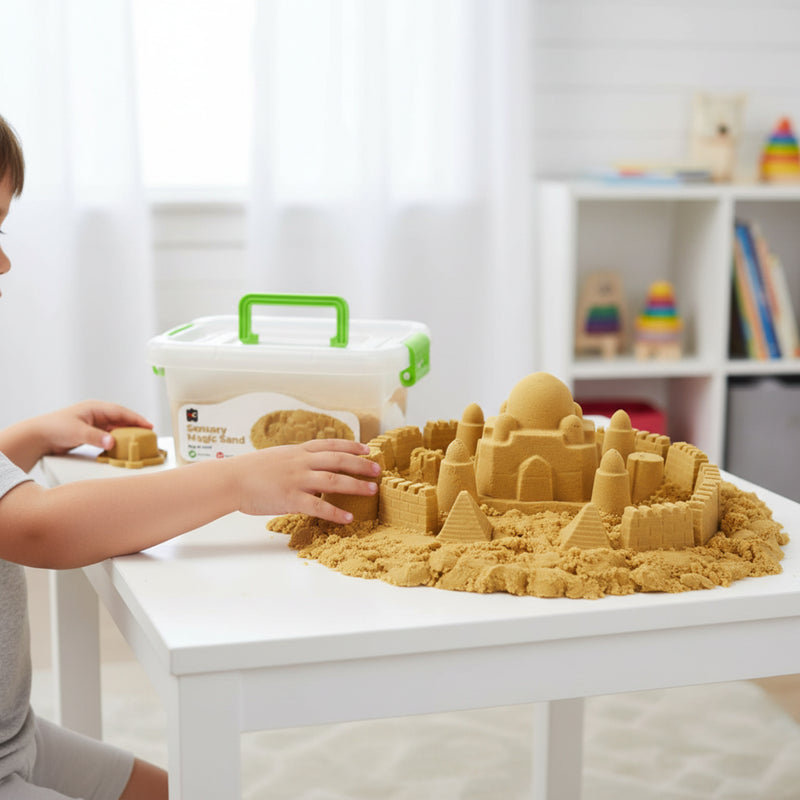 Young child creating an elaborate sandcastle city using natural sensory magic sand on a classroom table with moulded towers, walls, and pyramids displayed around the reusable storage container.