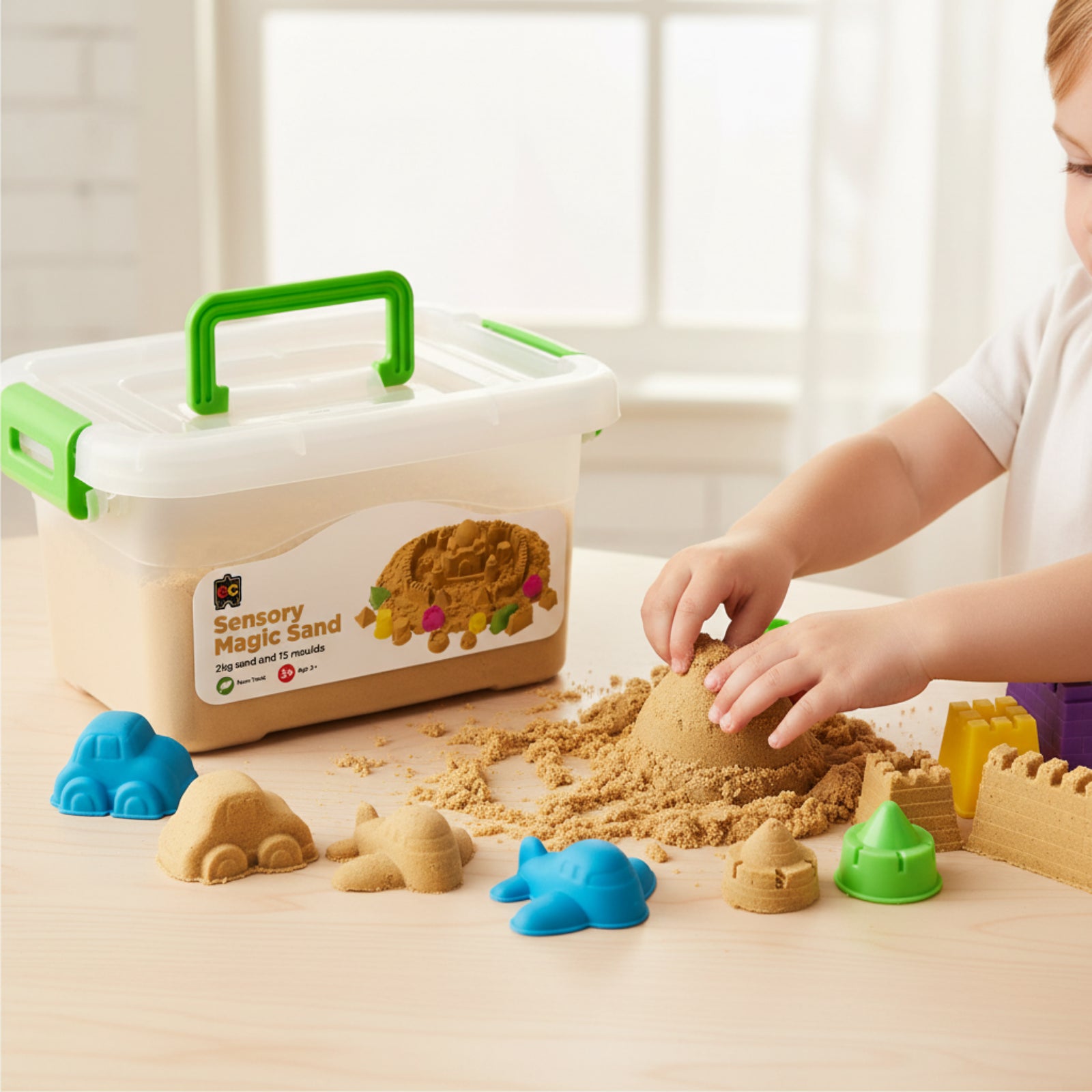 Child using Educational Colours Sensory Magic Sand with Moulds 2kg Natural while shaping sand structures beside colourful mould accessories and reusable storage tub.
