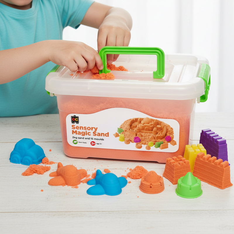 Young child placing orange sensory magic sand into reusable storage tub with colourful castle moulds and shaping accessories arranged on tabletop.