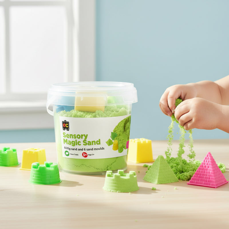 Young child enjoying tactile sensory play with green magic sand while colourful moulds and reusable storage tub sit on wooden table.