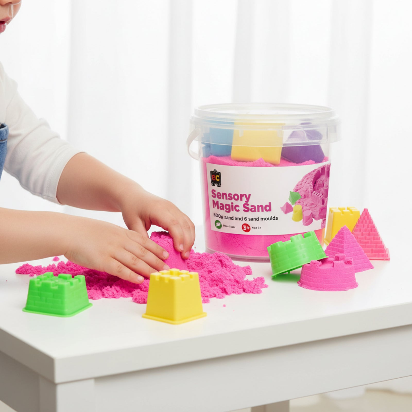 Child playing with bright pink Educational Colours Sensory Magic Sand while shaping moulds on a white activity table beside colourful accessories.