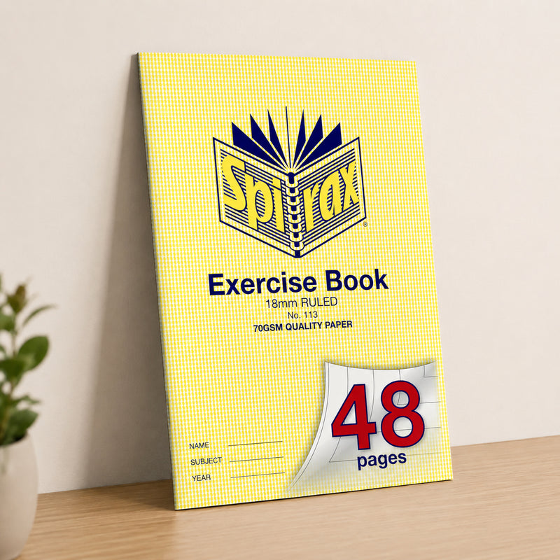 Spirax 113 A4 48 page exercise book standing upright against a neutral wall on a wooden desk with a plant nearby, presenting the yellow cover and 18mm ruled format in a clean lifestyle scene.