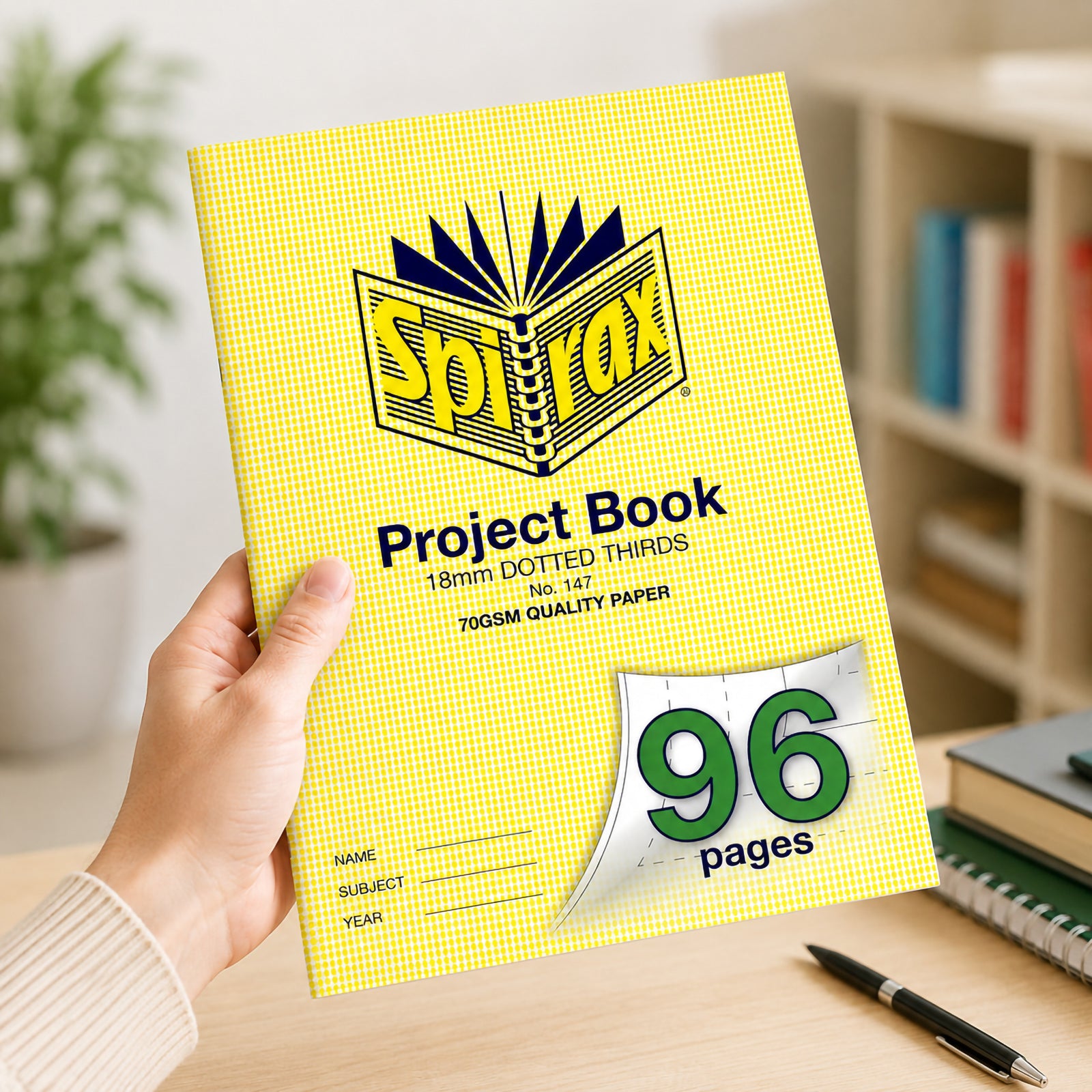 Person holding the Spirax 147 A4 Project Book with 96 pages and 18mm dotted thirds ruling in a bright study area, highlighting the durable yellow cover and generous writing capacity for classroom projects.