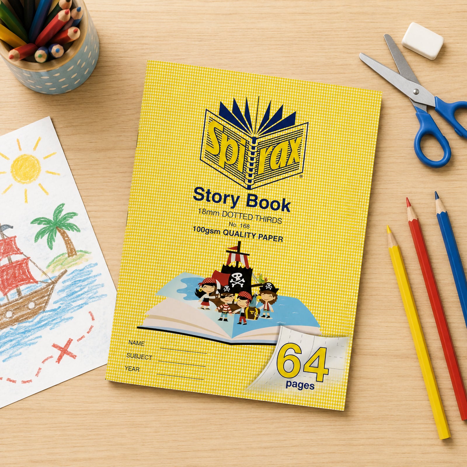 Top view of the Spirax 168 Story Book on a wooden desk surrounded by coloured pencils, scissors, eraser and a child's pirate drawing, showcasing an engaging literacy and art learning environment.