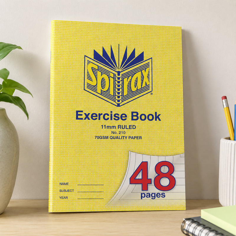 Spirax 210 A4 Exercise Book standing upright against a neutral wall on a tidy study desk beside stationery and indoor plants, presenting the notebook in a modern classroom or home study setting.