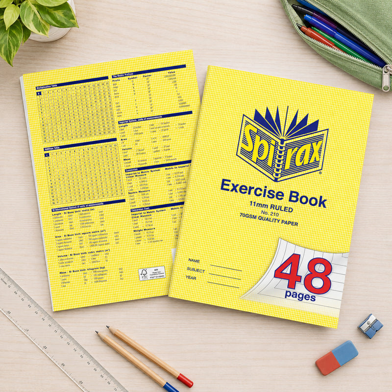 Top view showing the front and back of the Spirax 210 Exercise Book on a wooden desk with ruler, pencils, erasers and pencil case, highlighting both the classic cover and the useful educational reference tables printed on the back.