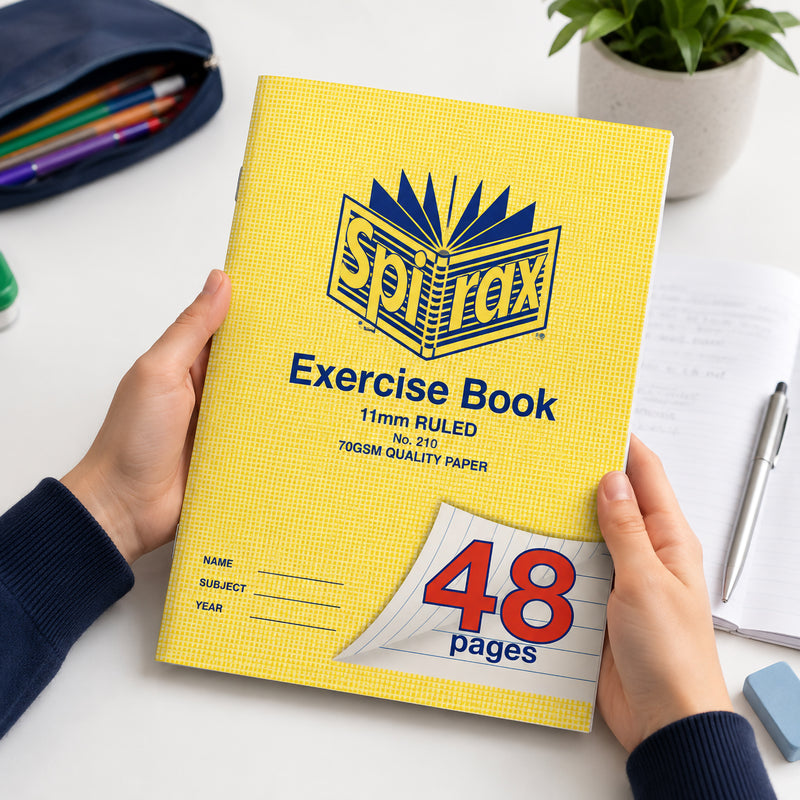 Student holding a Spirax 210 A4 Exercise Book with 48 ruled pages while studying at a desk with stationery and notebooks nearby, demonstrating its comfortable size for everyday classroom learning and homework.