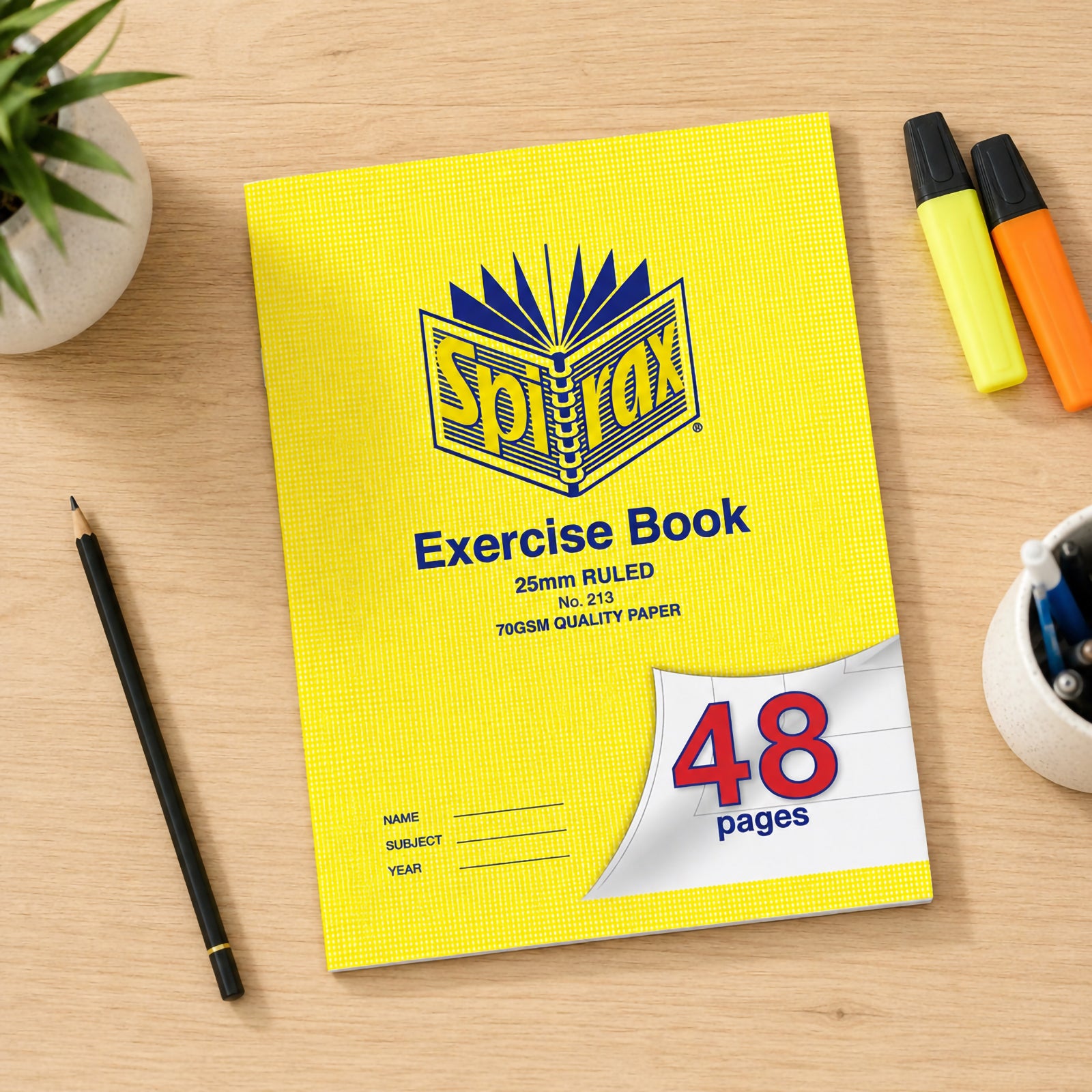 Top view of the Spirax 213 Exercise Book on a wooden desk with pencil, highlighters, stationery cup and plant, presenting the classic yellow cover and 48 page capacity for early classroom writing.