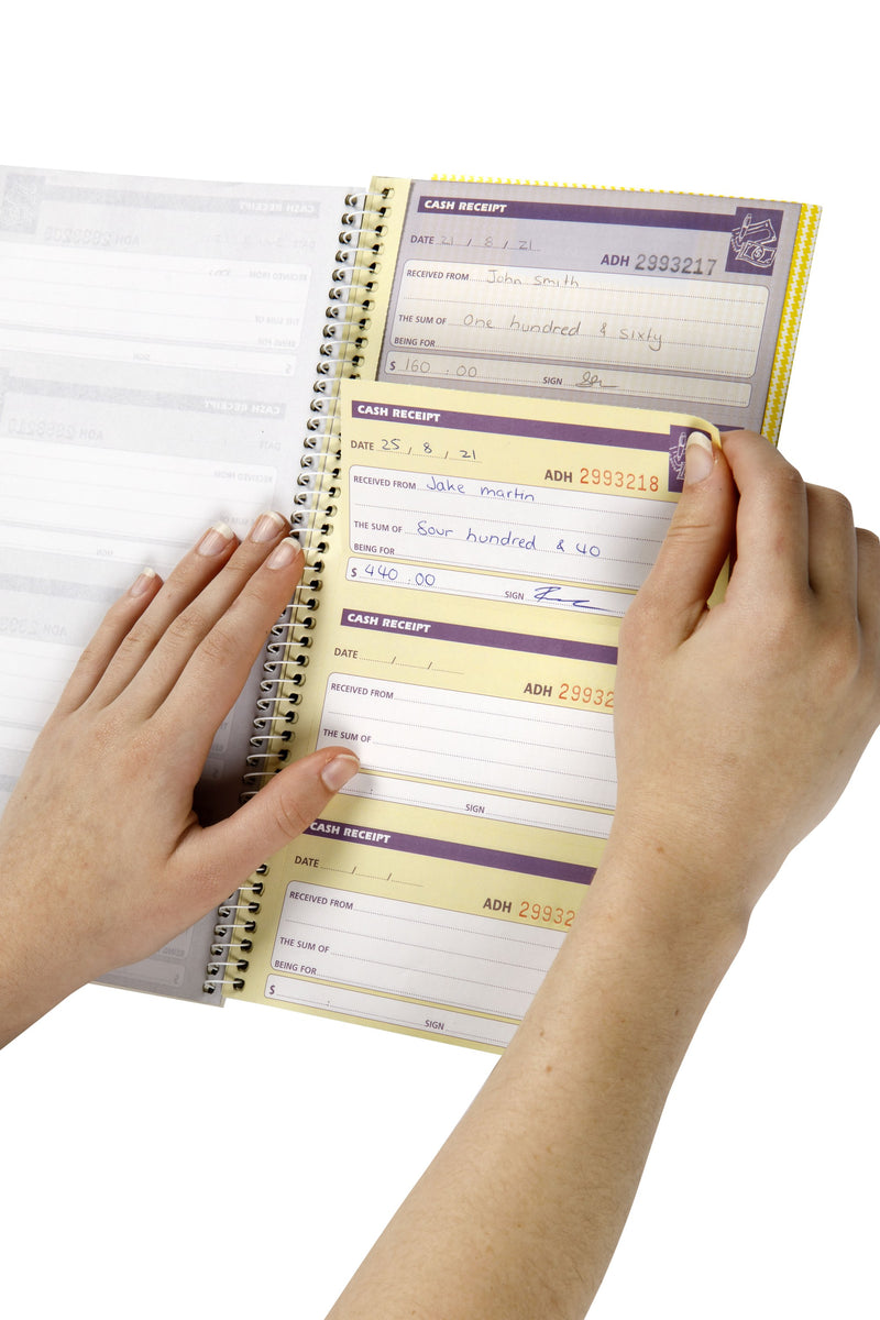 Hands tearing a completed cash receipt out of a Spirax No. 553 cash receipt book, with the duplicate copy of the receipt kept in the book