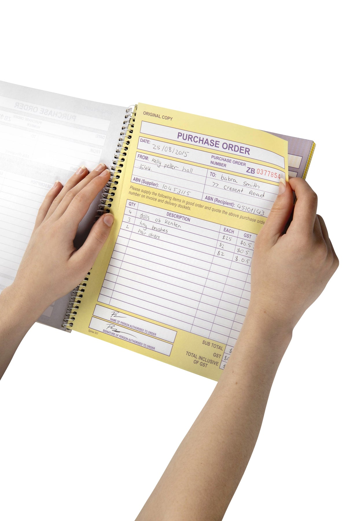 Two hands holding a Spirax 501 carbonless book open at a handwritten yellow purchase order form, with the spiral binding along the left edge