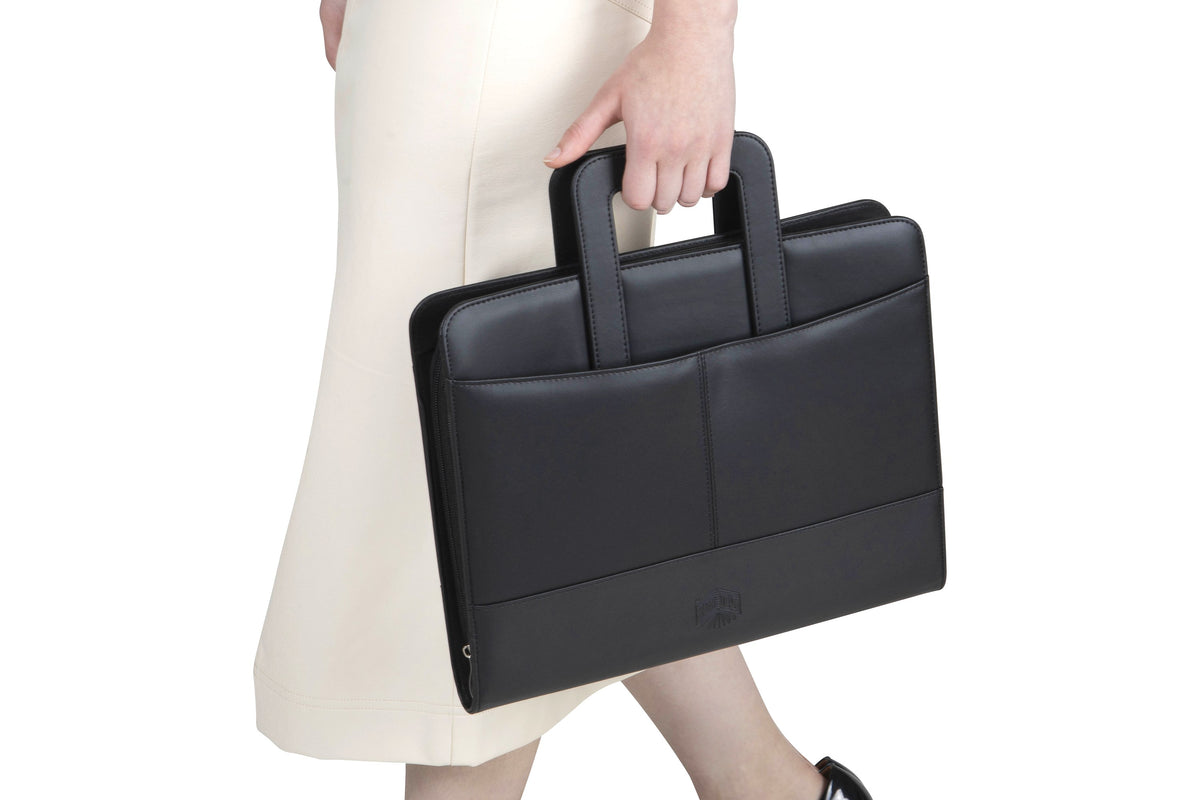 Spirax executive compendium carried by one of its handles, closed and zipped, held at the side of a person in a cream skirt