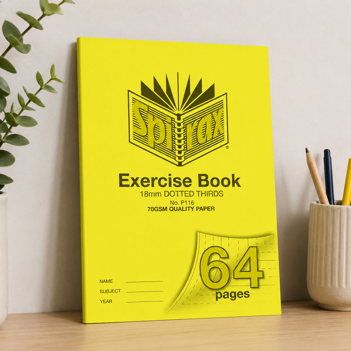 Yellow Spirax P116 A4 exercise book leaning against a pale wall on a timber desk beside a pot of pencils and a plant
