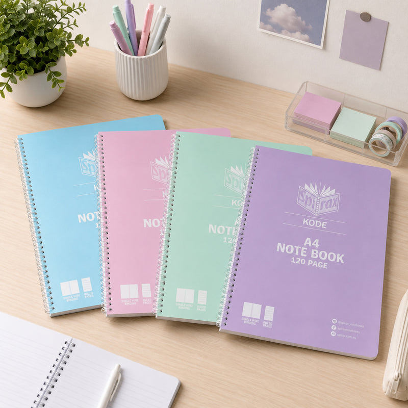 Assorted Spirax Kode A4 metallic notebooks in pastel blue, pink, mint and purple displayed on a wooden study desk with pens, sticky notes, plant and stationery, showing a bright organised workspace for school or study.