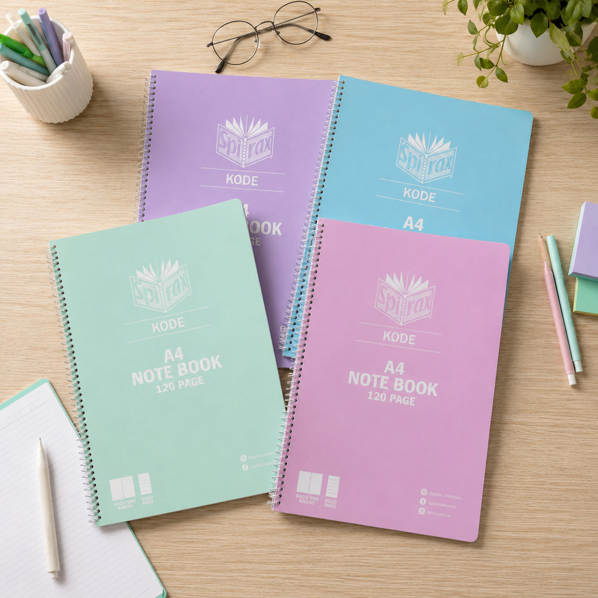 Top view of four Spirax Kode A4 metallic notebooks on a timber desk with pens, glasses and sticky notes