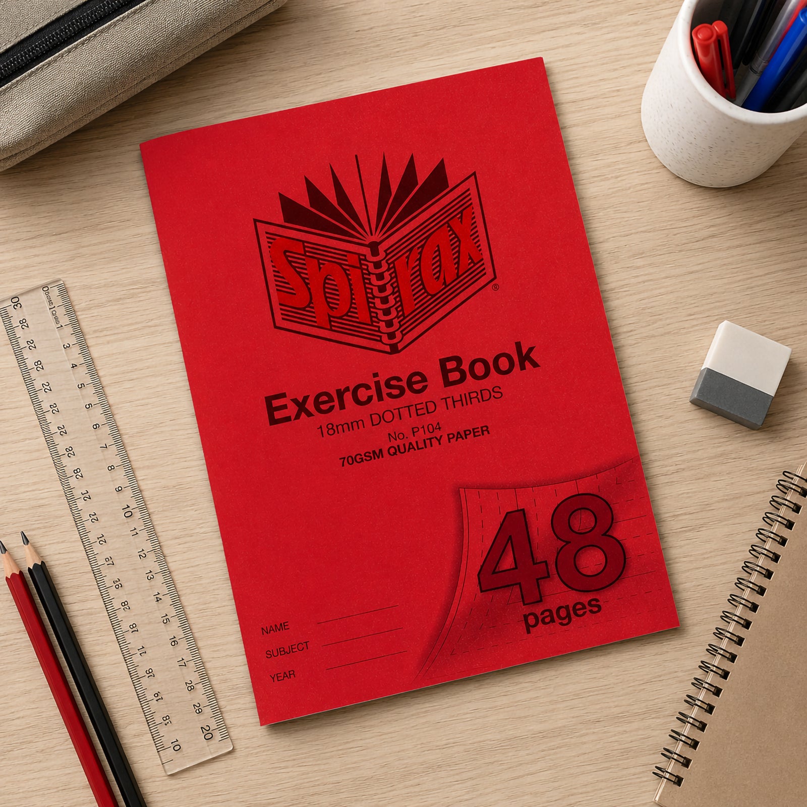 Top view of the Spirax P104 A4 exercise book placed neatly on a timber desk with pencils, ruler, eraser, notebook and pencil case, presenting an organised classroom workspace that showcases the 18mm dotted thirds exercise book.