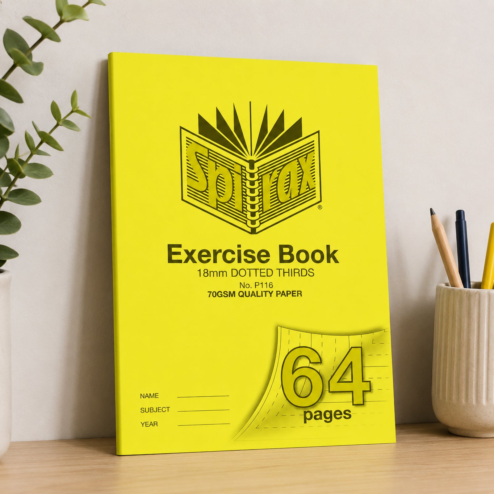 Spirax P116 A4 exercise book standing against a neutral wall on a timber desk with pencils and indoor plants, highlighting the bright yellow cover and durable classroom ready design.