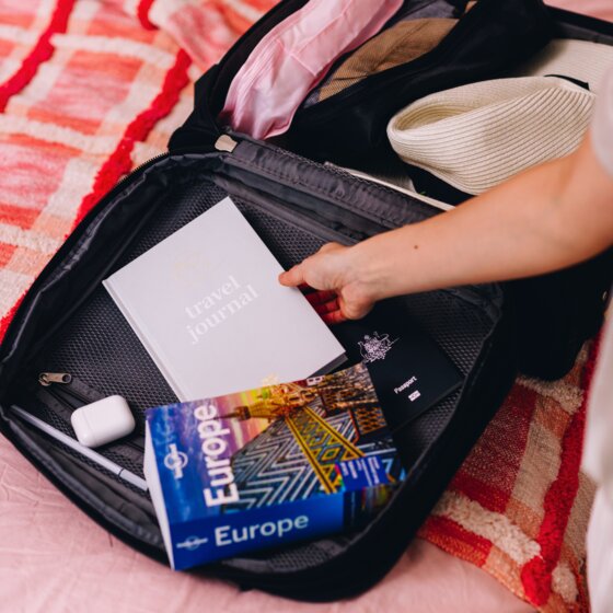 Hand placing a cloud Spirax travel journal into an open suitcase next to a Europe travel guide