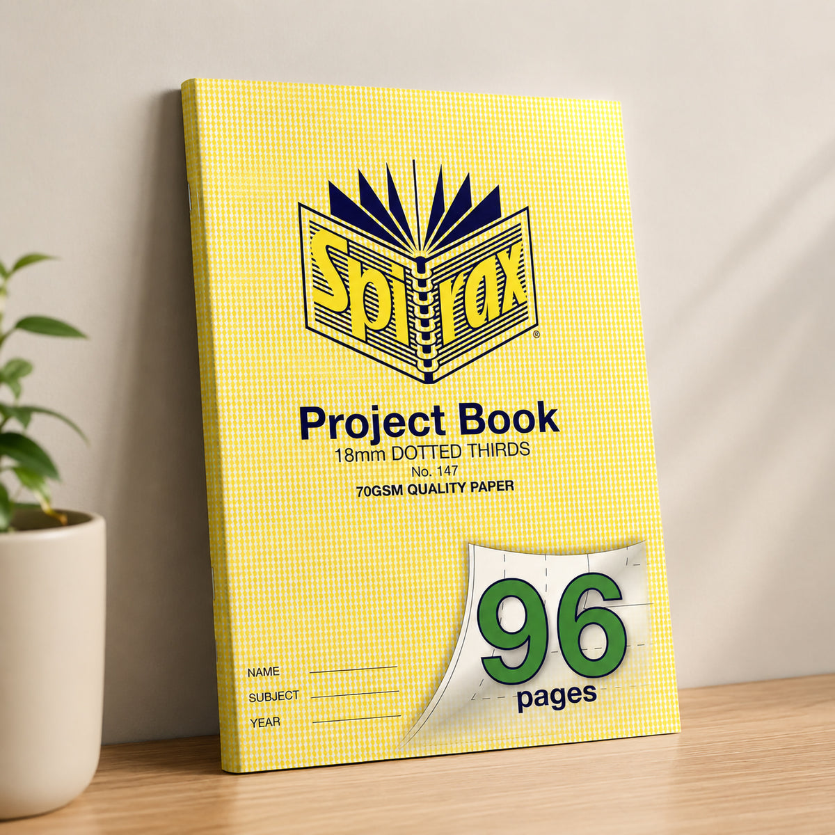 Spirax 147 project book leaning upright against a neutral wall on a wooden desk next to a potted plant
