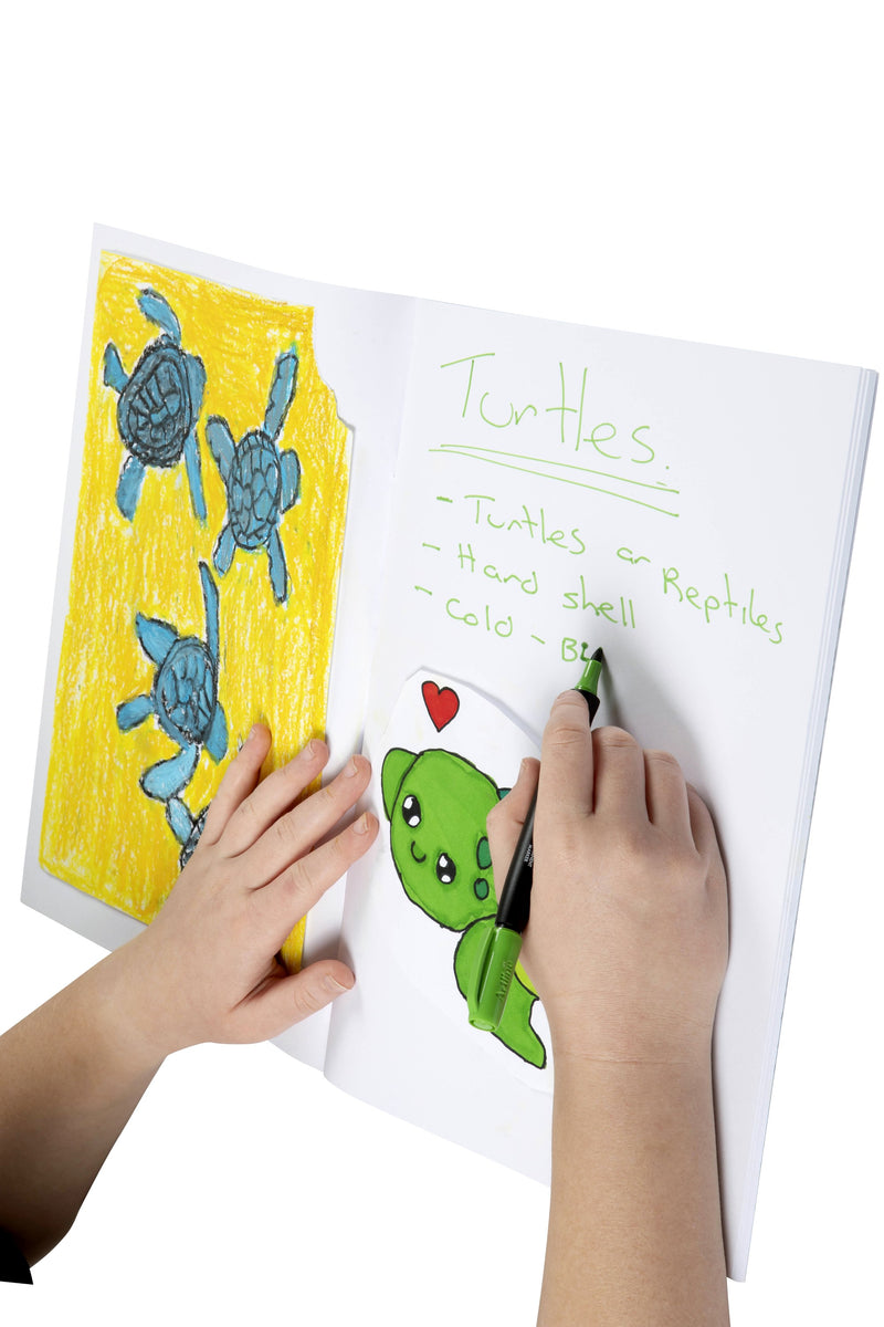 Child writing turtle facts in green marker in an open Spirax 152 scrapbook, beside a coloured drawing of turtles and a cartoon turtle cut-out