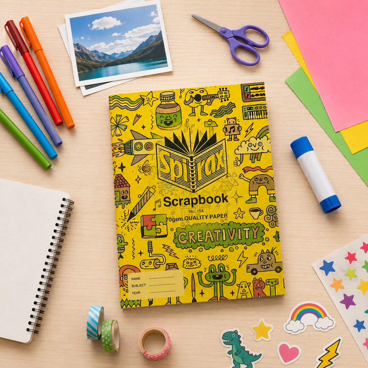 Spirax 154 scrapbook lying on a desk among felt pens, a glue stick, scissors, washi tape, stickers and coloured paper