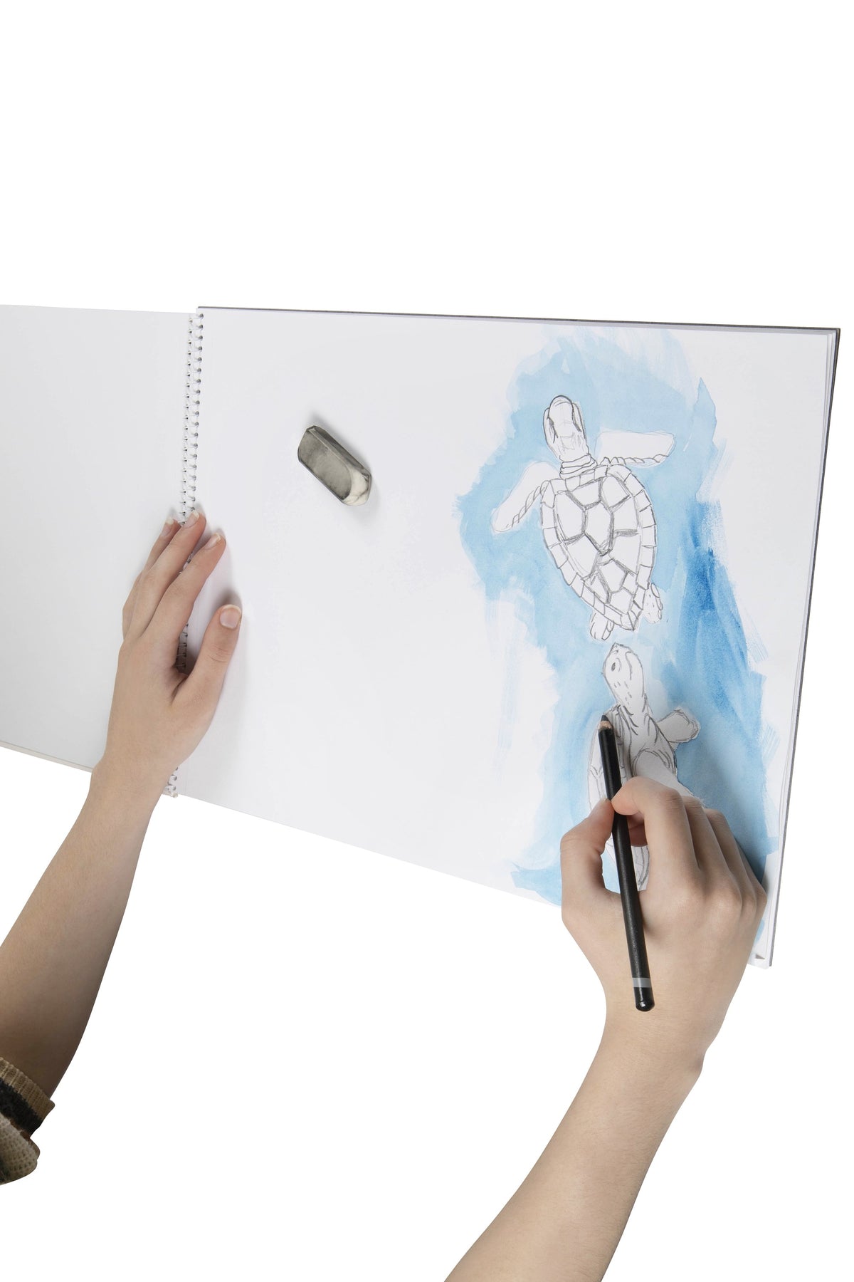 Hand drawing sea turtles over a blue watercolour wash on a page of an open Spirax 533 A3 sketch book, with an eraser resting on the page