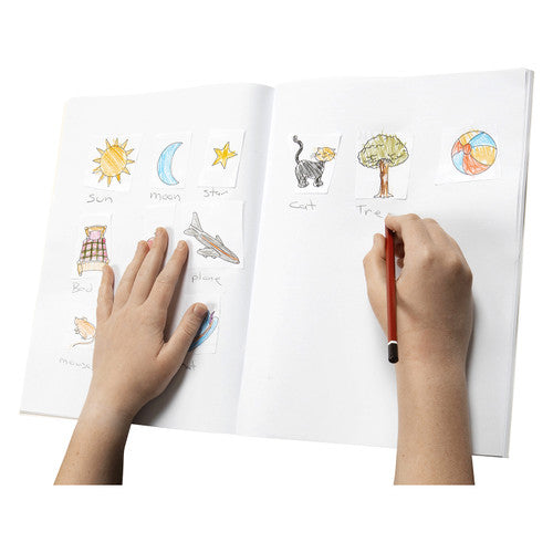Hands writing labels beside cut out pictures of a sun, moon, cat and tree pasted across the blank pages of an open Spirax scrapbook
