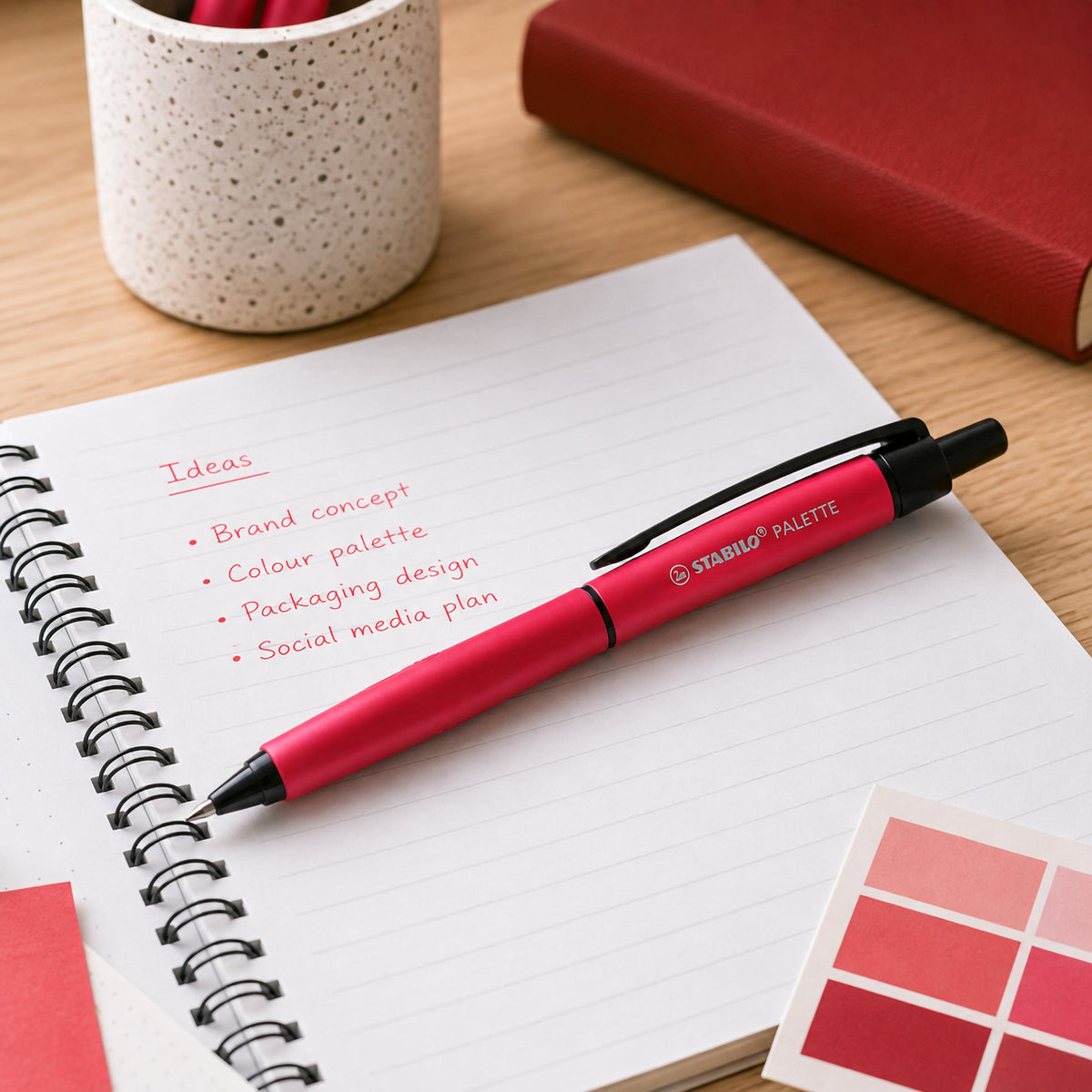 The STABILO Palette Retractable Rollerball Gel Pen Red displayed across an open notebook with planning notes and colour samples. The image showcases the pen as an ideal writing instrument for creative projects, journaling, study and office organisation.