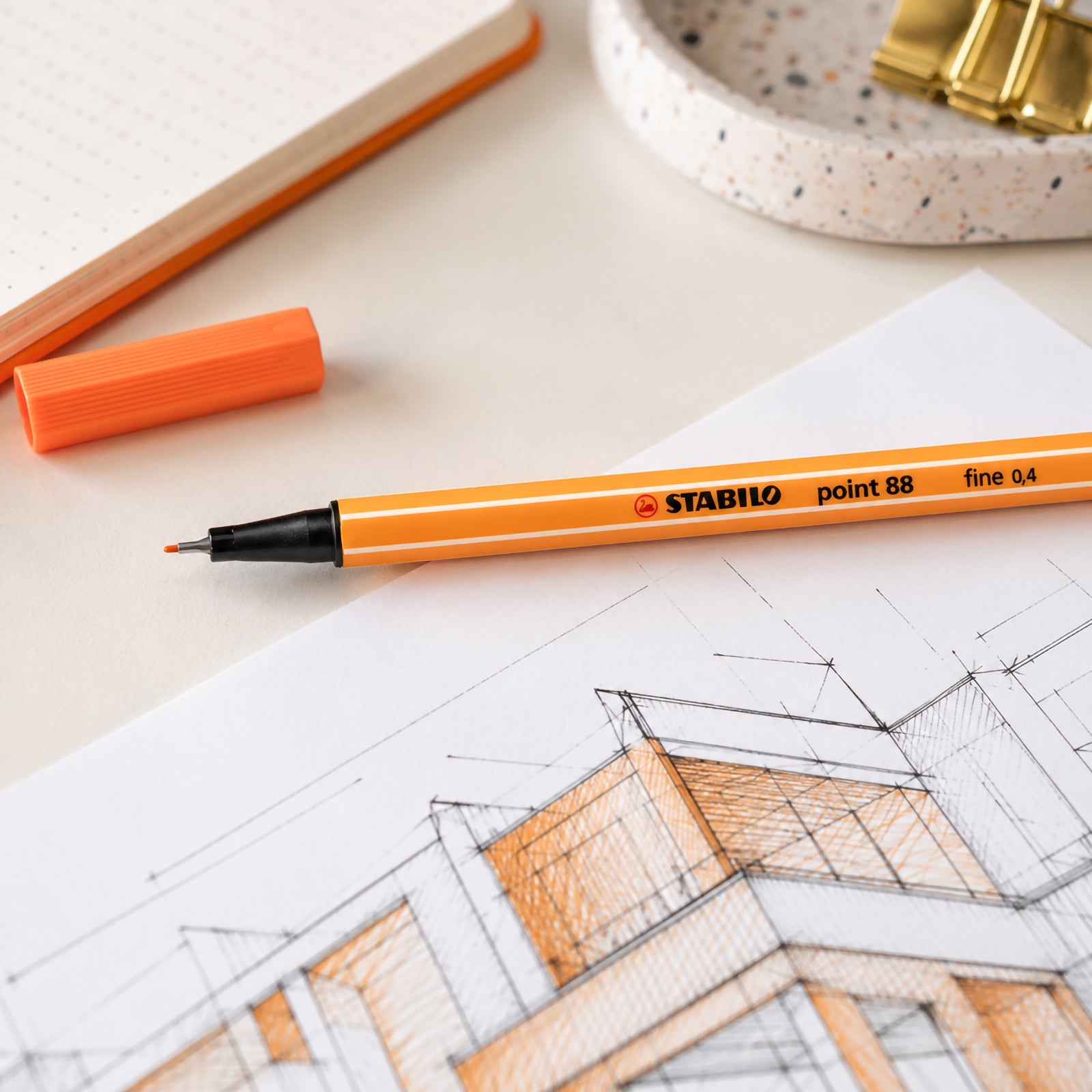 Close up of the Stabilo Point 88 Fineliner Apricot resting across an architectural drawing. The fine 0.4 mm metal enclosed tip is clearly visible beside the matching apricot cap, emphasising accuracy and premium design.