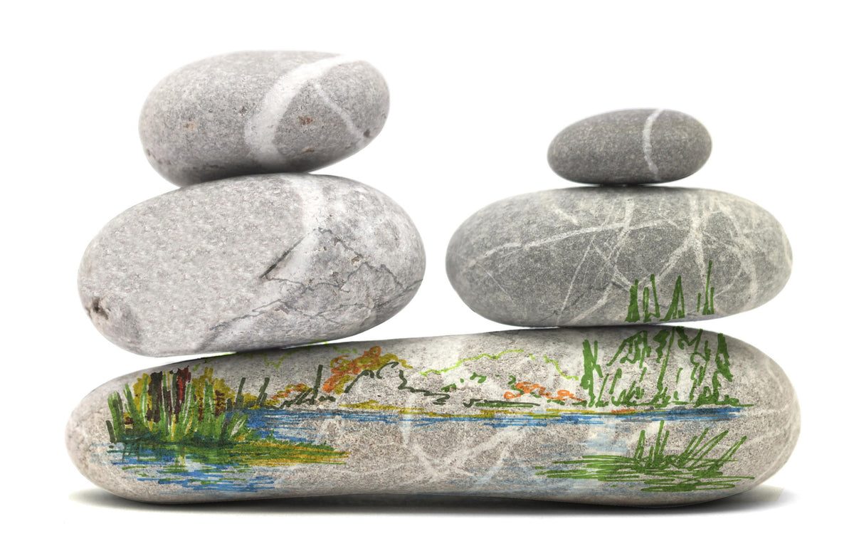 Stacked grey pebbles with a lake and reed band painted along the bottom stone, first stage of a pen artwork