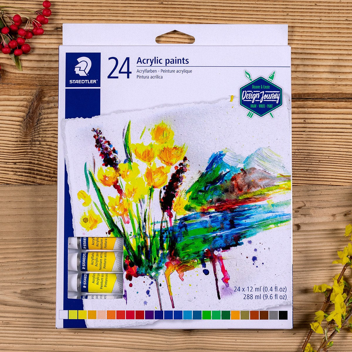 Staedtler 8500 box of 24 acrylic paints lying on a wooden table with yellow flowers and red berries