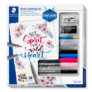 Staedtler Design Journey Brush Lettering Set box with a floral be a free spirit lettering card, and a window showing the sharpener, eraser, pencil and six pens