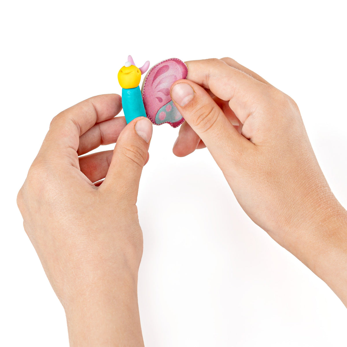 Fingers pressing a pink wing onto a turquoise clay butterfly body