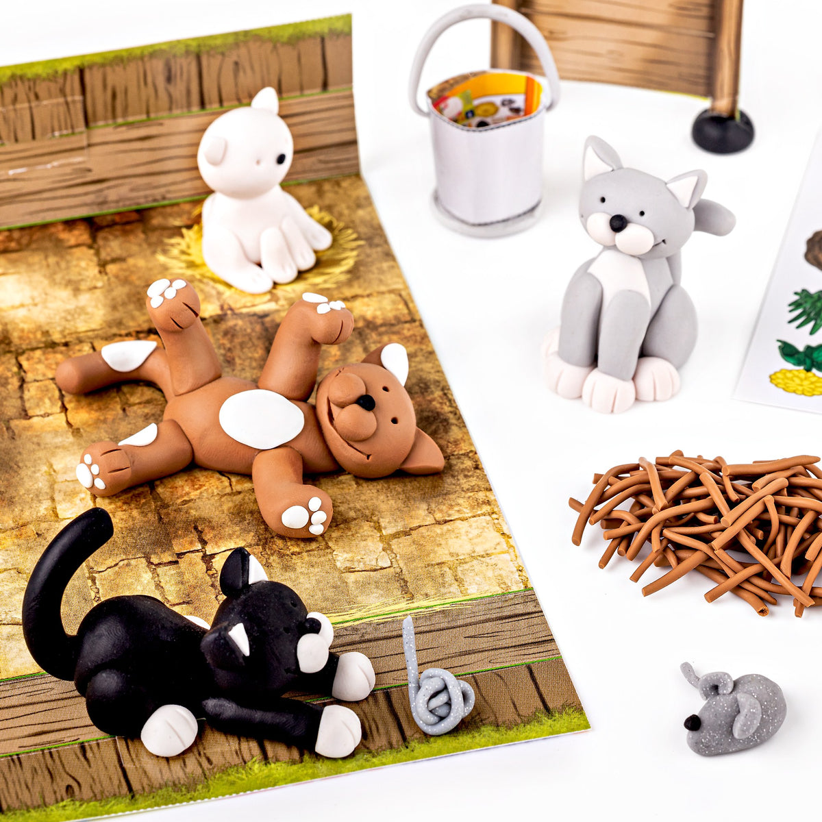 Clay cats in white, grey, brown and black with a small mouse, straw and a bucket on a wooden floor scene