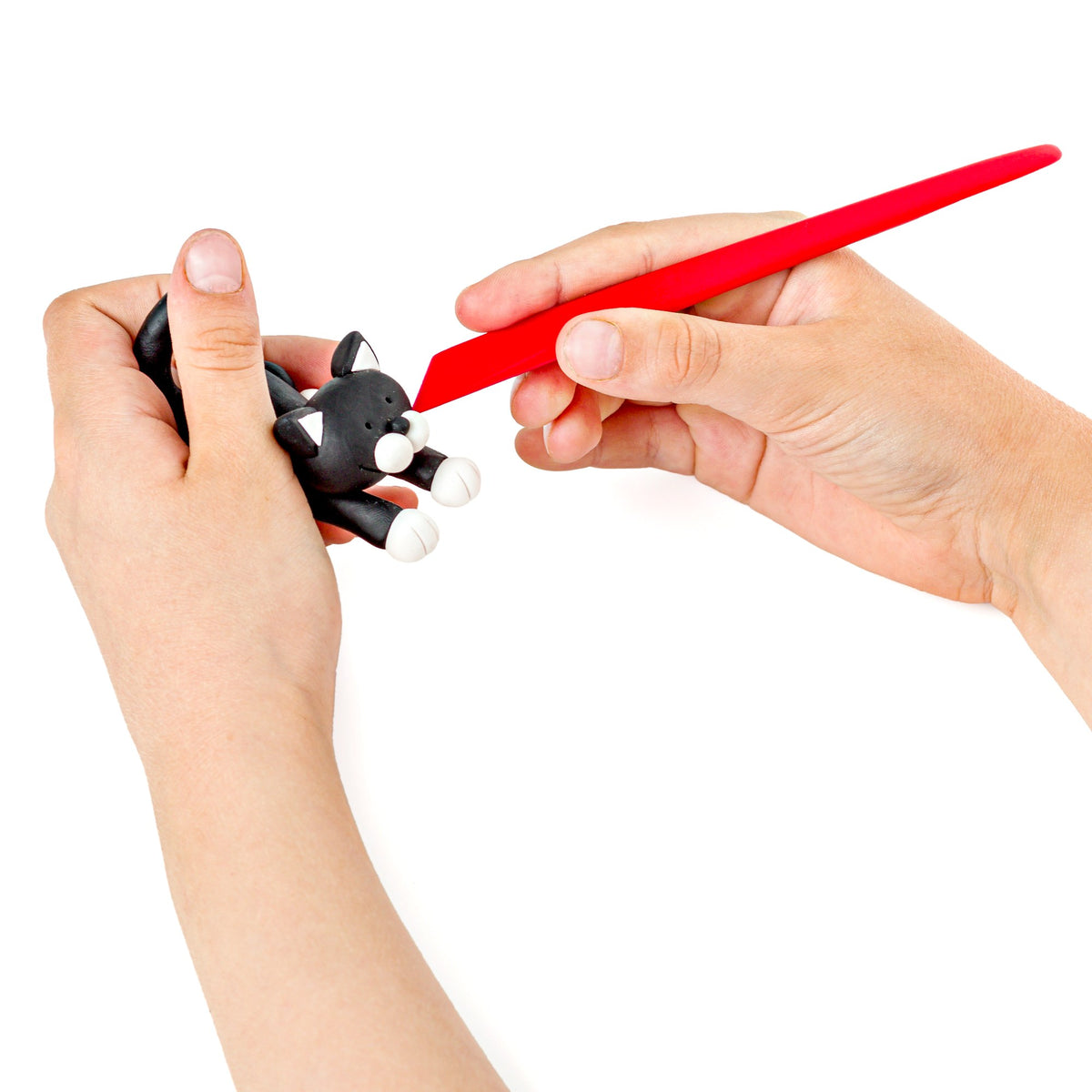 Hand holding a black clay cat and shaping its face with the red modelling stick