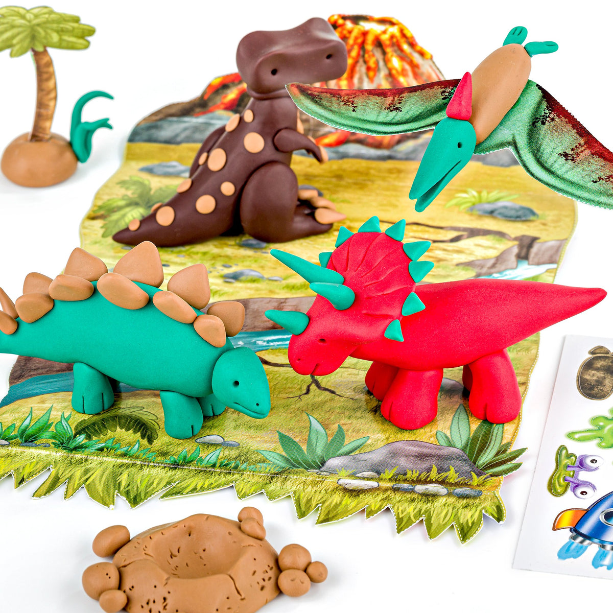 Clay dinosaurs in red, teal and brown plus a green flying reptile on a rocky play scene with palm trees and a volcano