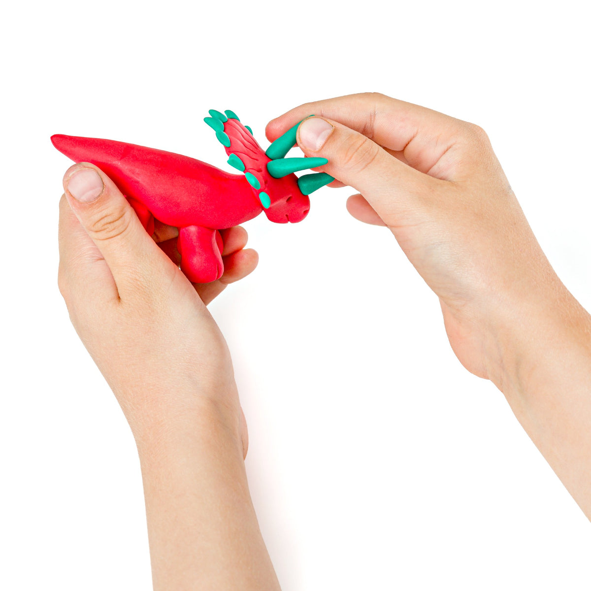 Fingers pinching red spikes onto a clay dinosaur while holding the red modelling stick