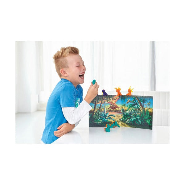 Boy laughing as he plays with clay dinosaurs in front of a jungle backdrop