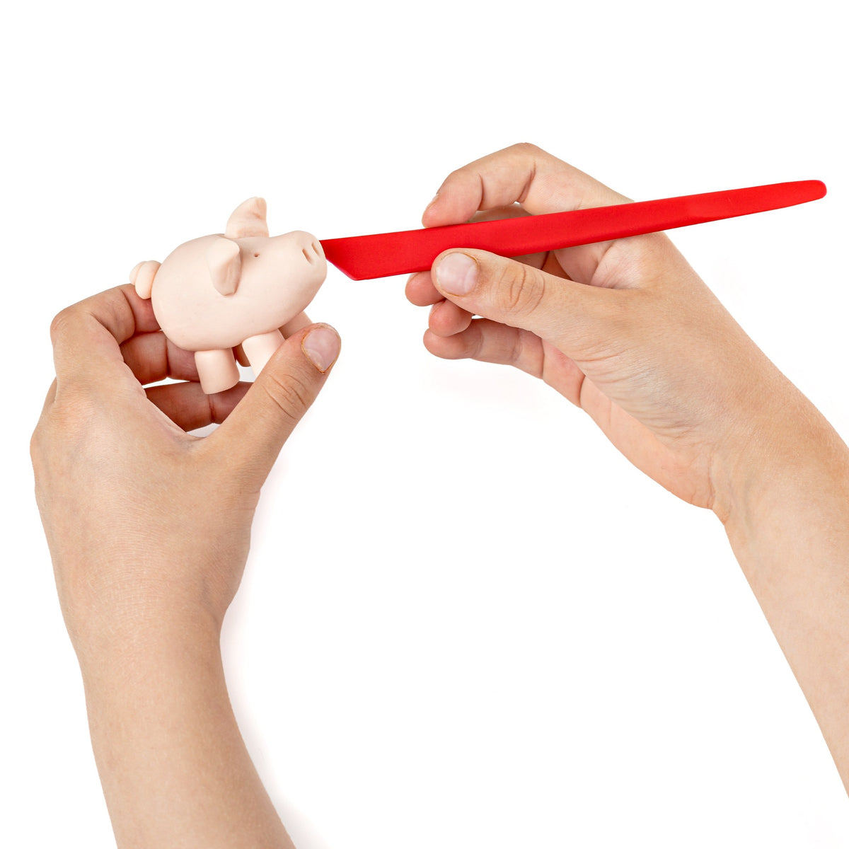 Child hand shaping a pink clay pig with the red modelling stick from the set