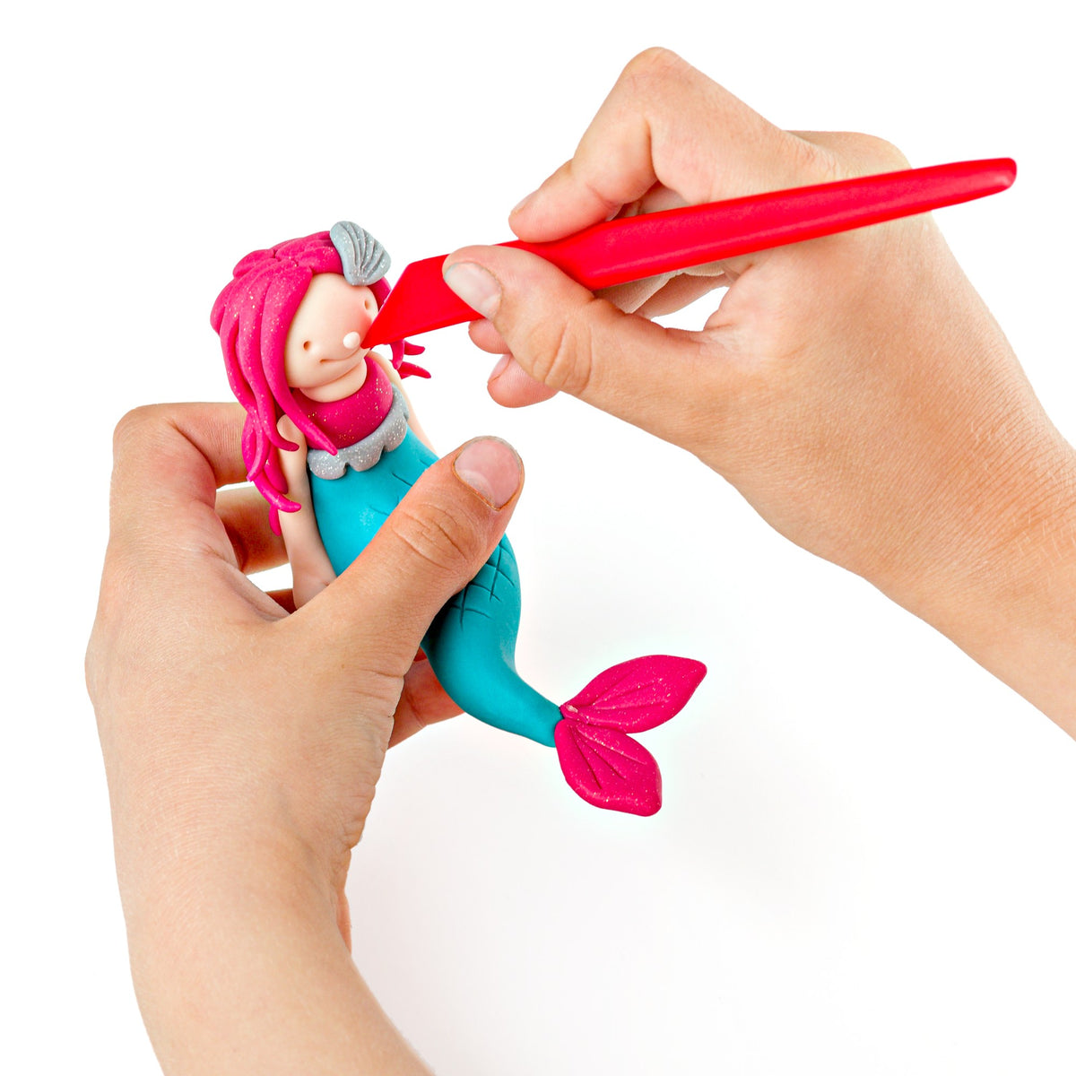 Hand adding a strand of pink hair to a clay mermaid with the red modelling stick