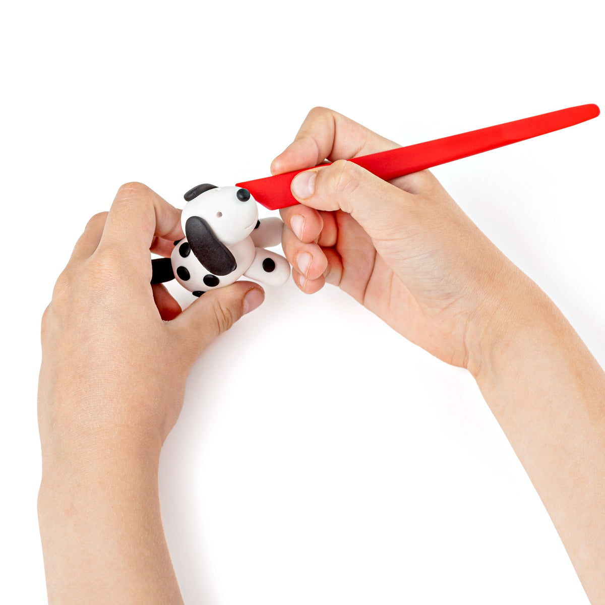 Hand smoothing a black and white spotted clay dog with the red modelling stick