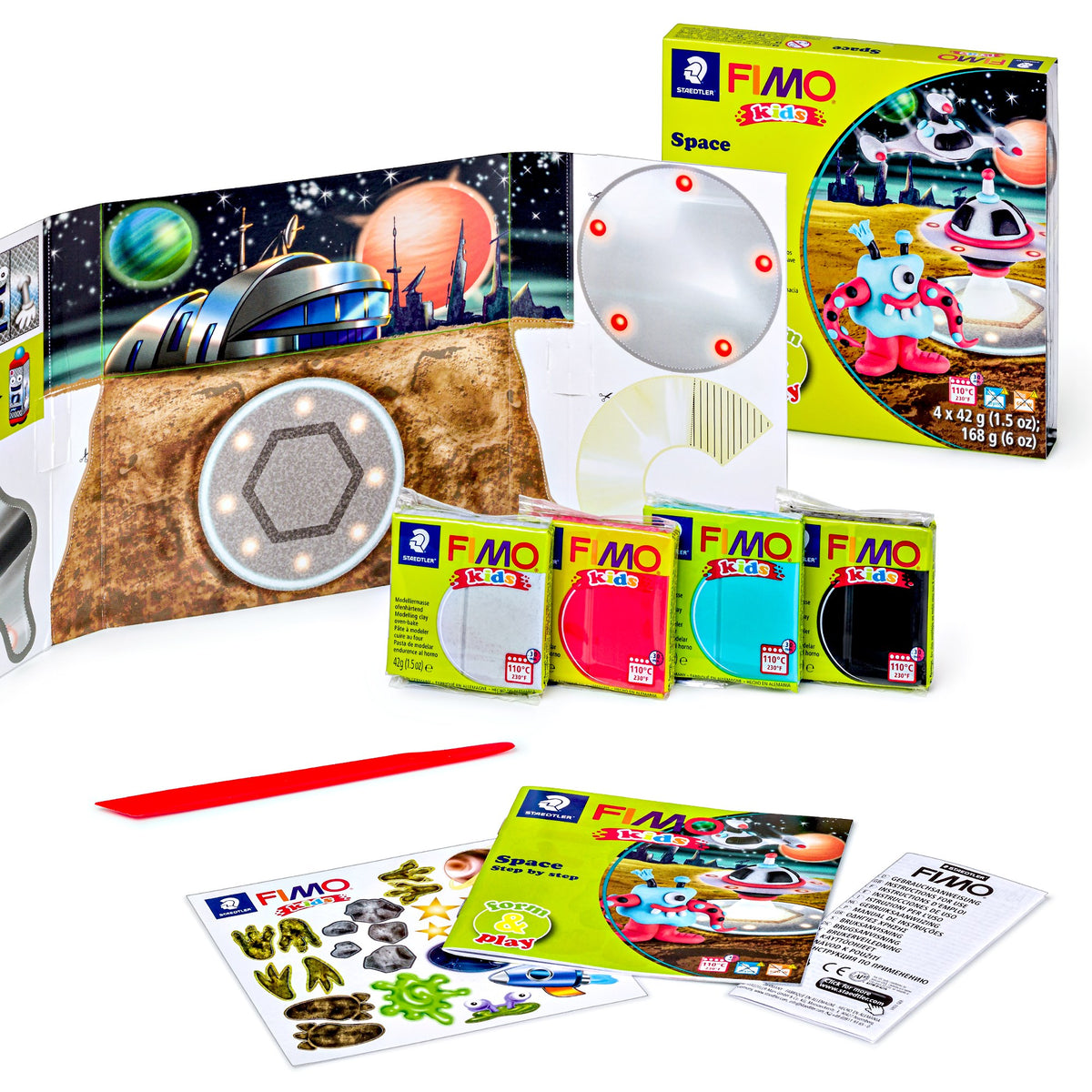 Contents of the FIMO kids Space set laid out: space backdrop, playing surface, four clay blocks, red modelling stick, sticker sheet and instruction leaflets