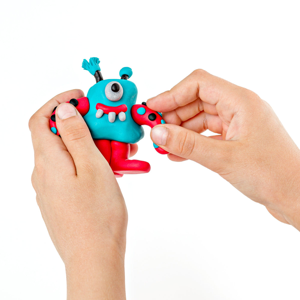 Two hands attaching a red arm to a turquoise one-eyed alien made from FIMO kids clay