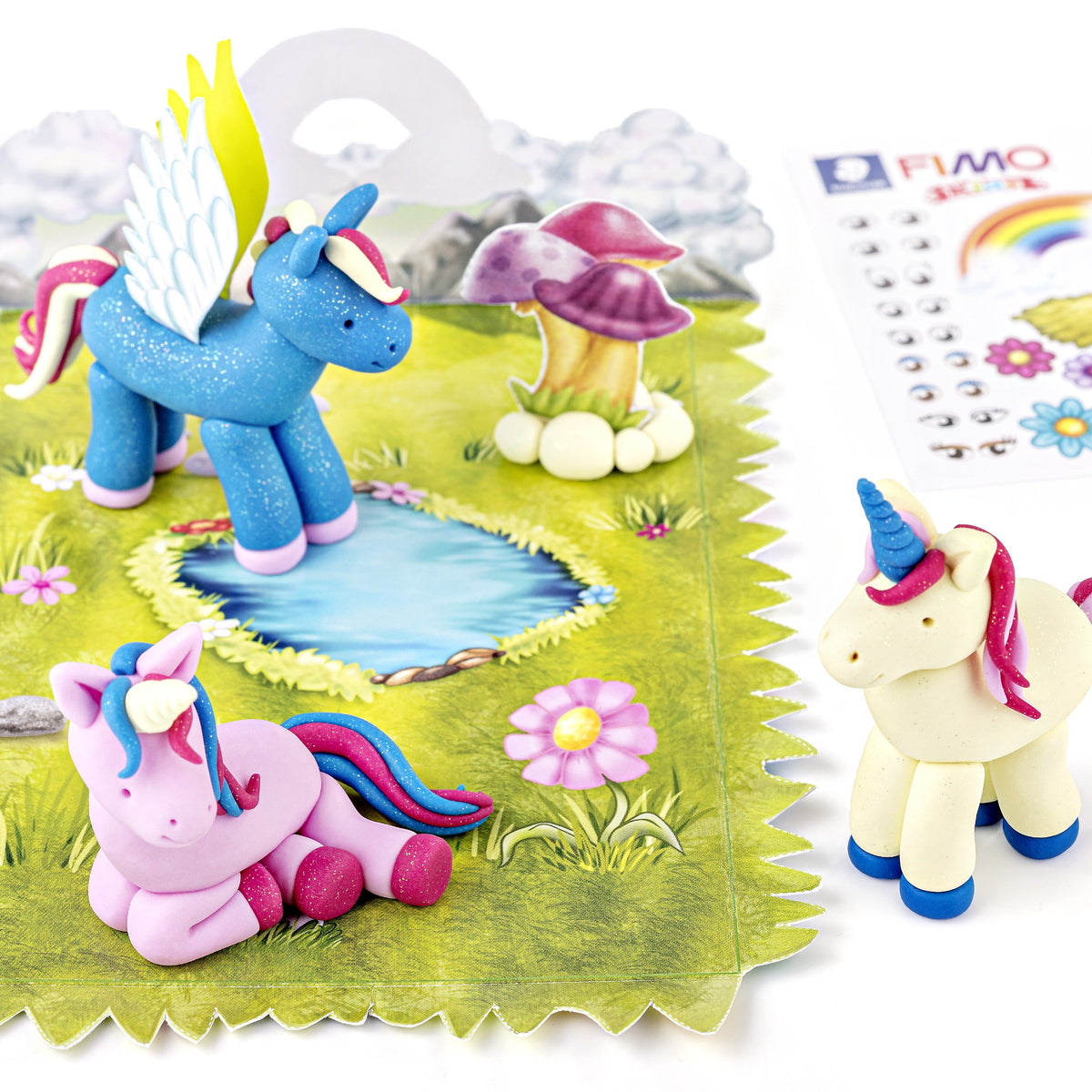 Finished unicorns from the set, one blue with wings, one pink lying down and one cream, standing by a pond on the meadow playing surface