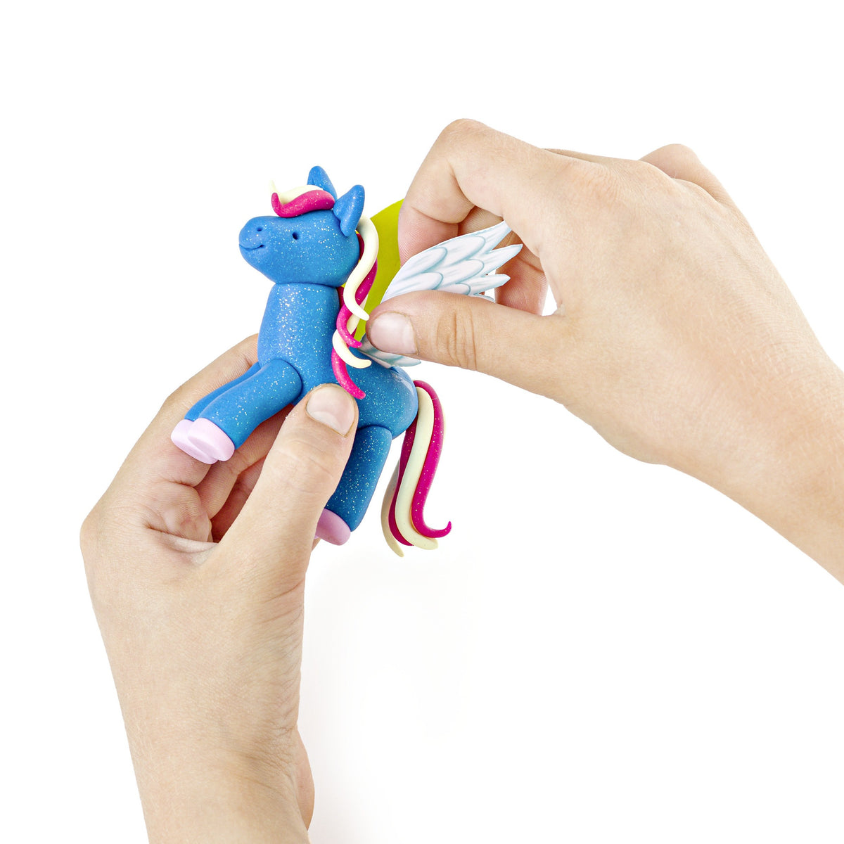 Two hands adding white wings to a glitter blue FIMO kids unicorn