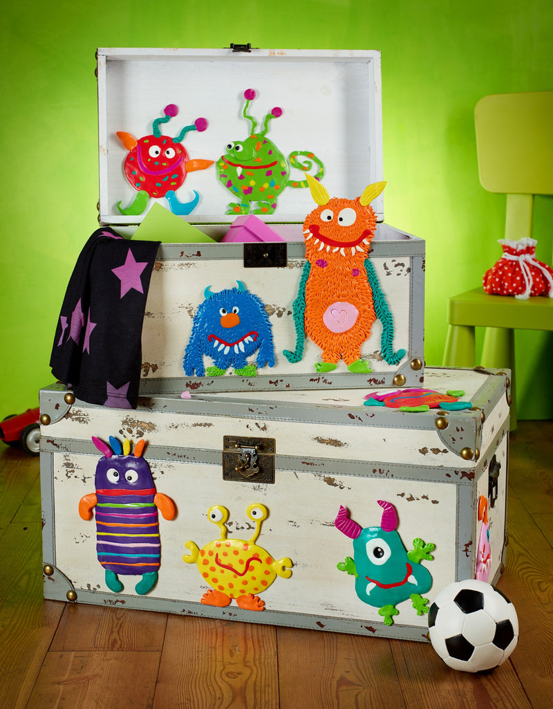 Staedtler photo of FIMO kids monster models in red, yellow, blue and green fixed to a painted wooden chest in a playroom