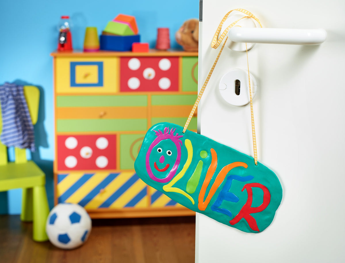 Staedtler photo of a turquoise FIMO kids door plaque spelling a child's name in coloured clay letters, hanging on a playroom door handle