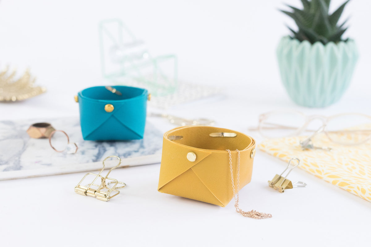 Staedtler photo of small folded FIMO leather-effect baskets in teal and mustard holding rings and trinkets on a white table