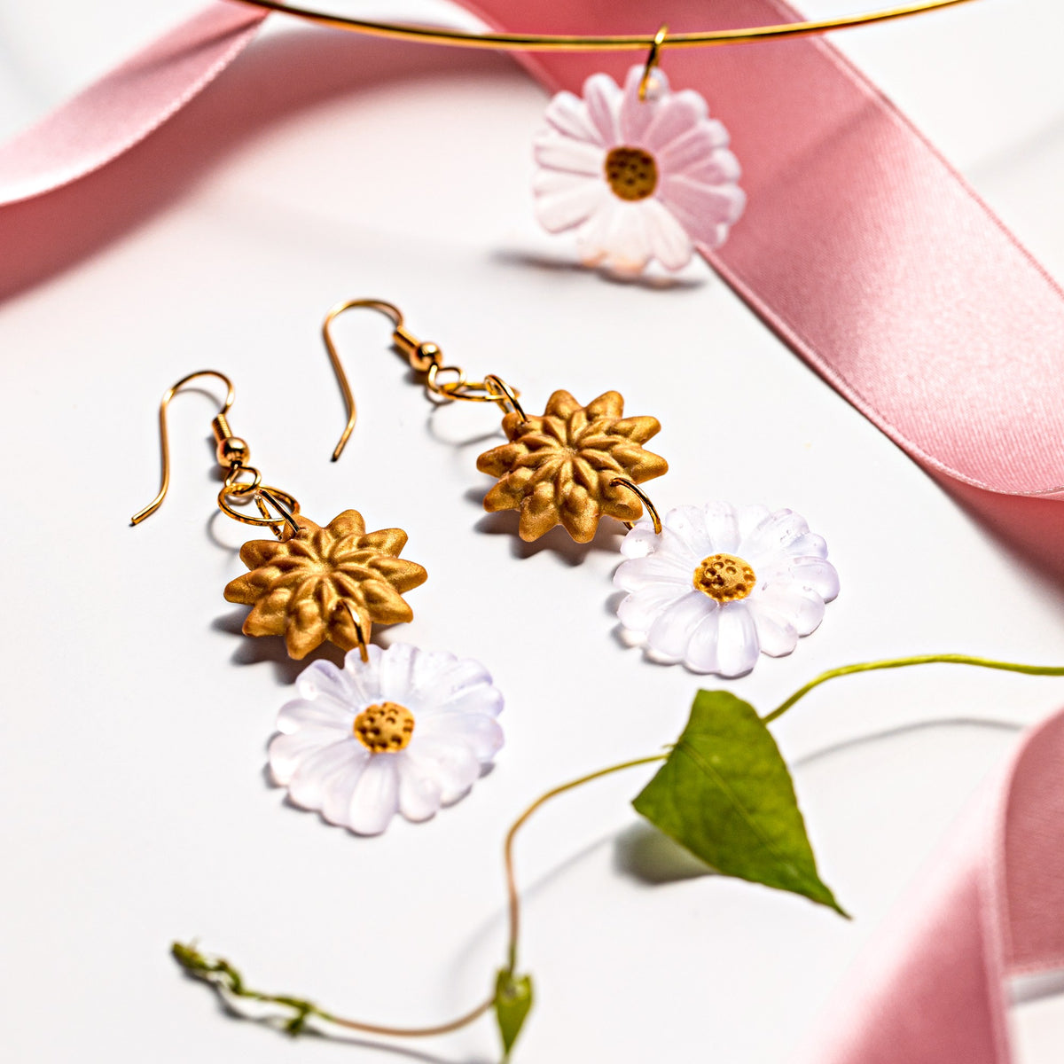 Flower earrings and a pendant from Staedtler's FIMO liquid project photos, with gold and translucent flowers hung on gold wire against pink ribbon